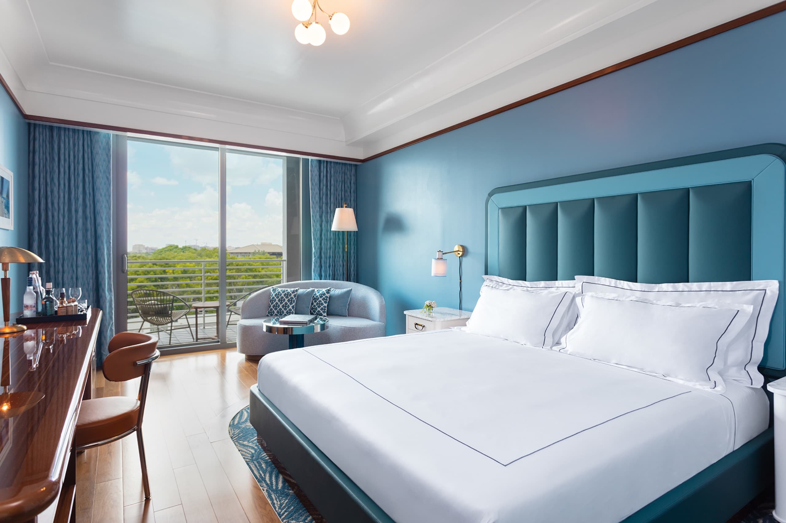 Premier King: king bed with padded blue headboard, patterned carpet and balcony over the greenery