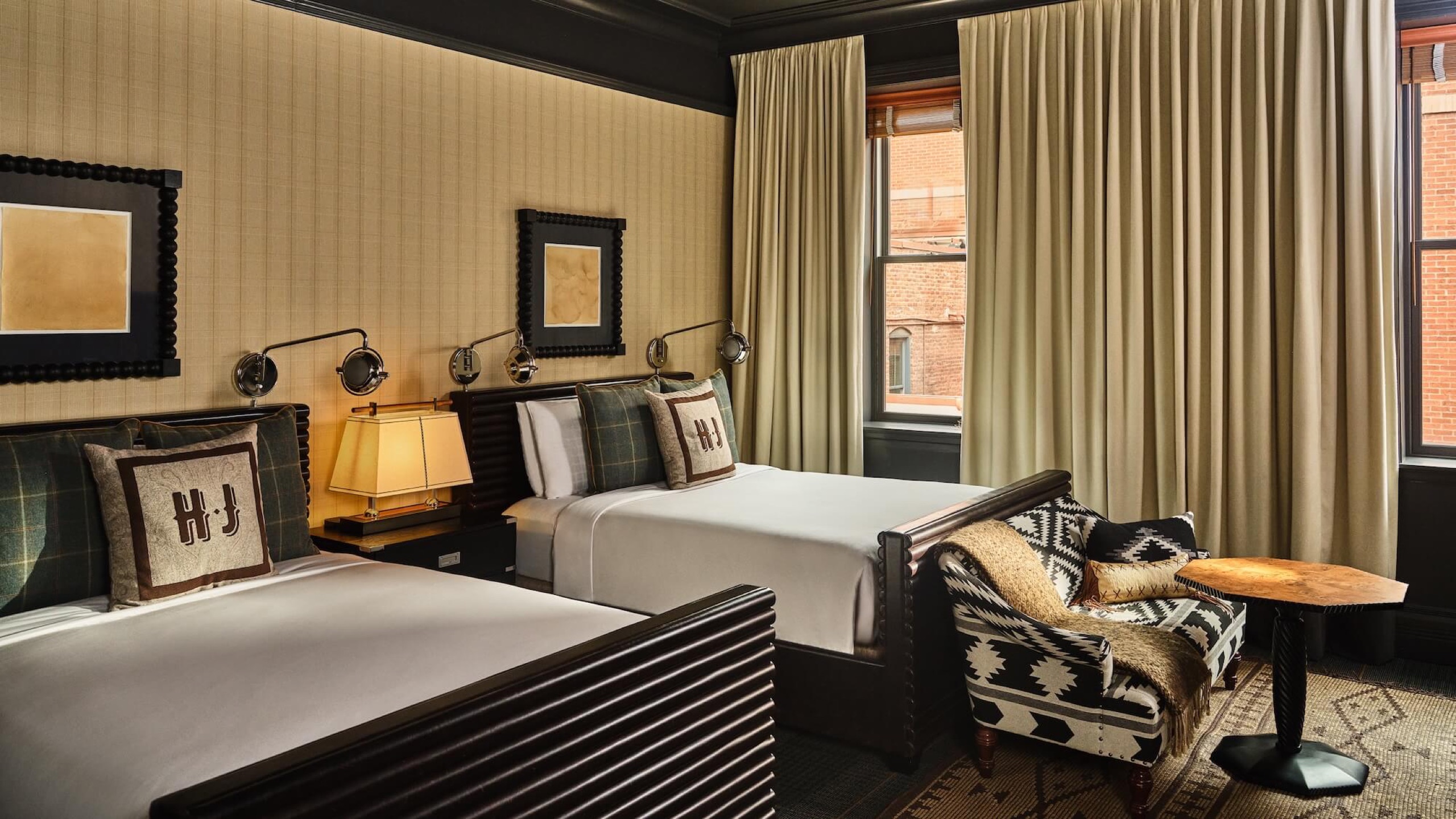 Junior Suite Double (650 sq ft) — two beds with plaid HJ pillows, Aspen brick rooftops through the window