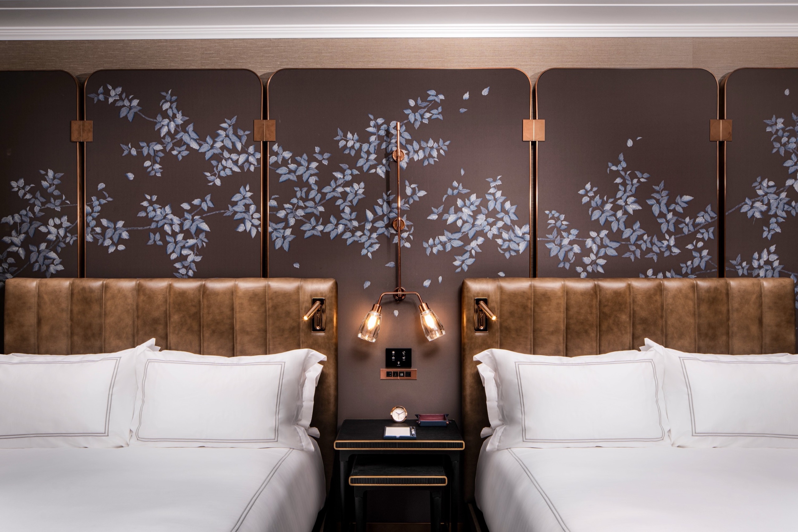 Deluxe Two Queens Room — twin queen beds with cognac leather headboards under the blossom-branch wall panels