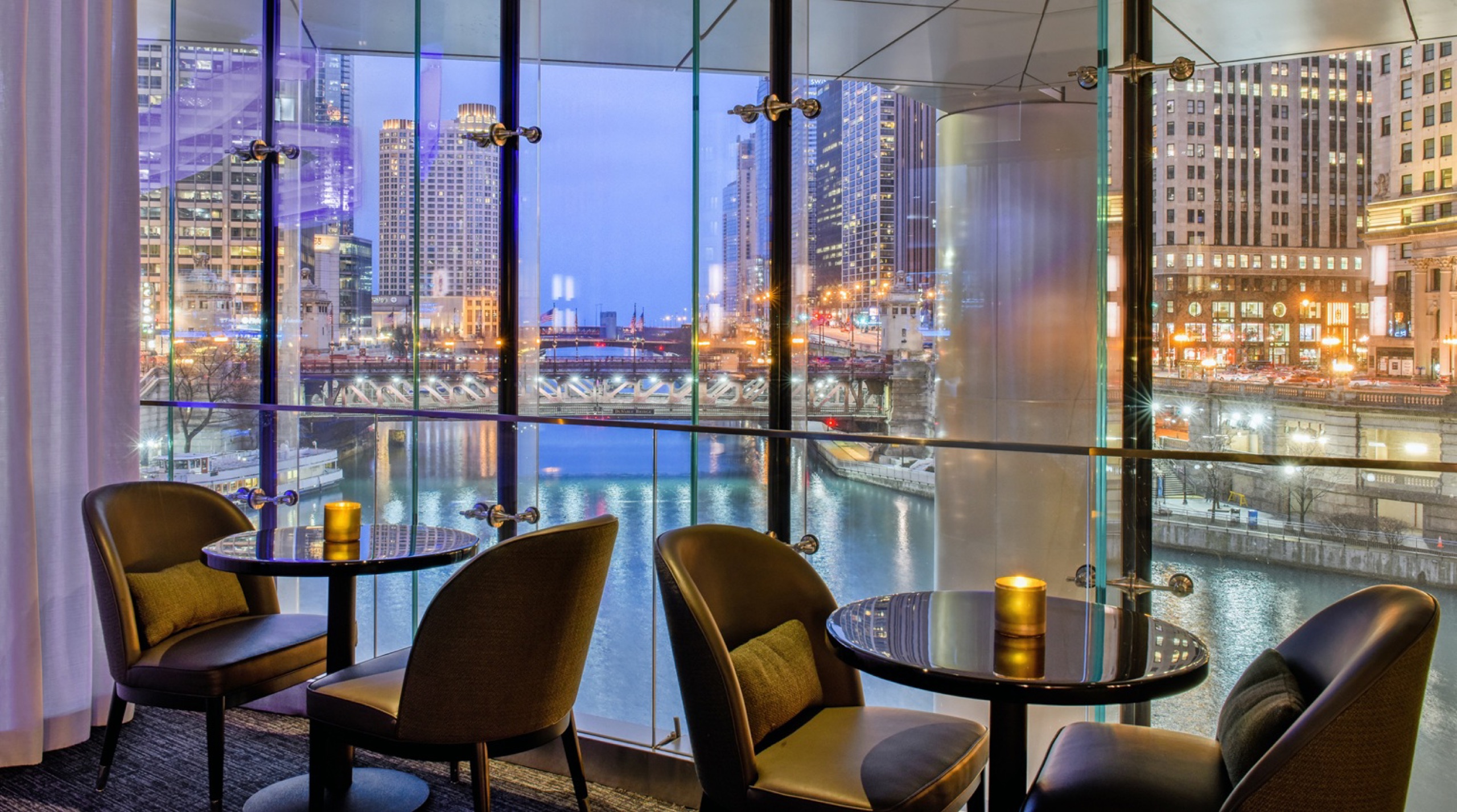 Rebar lounge at night, cocktail tables against the river-view window