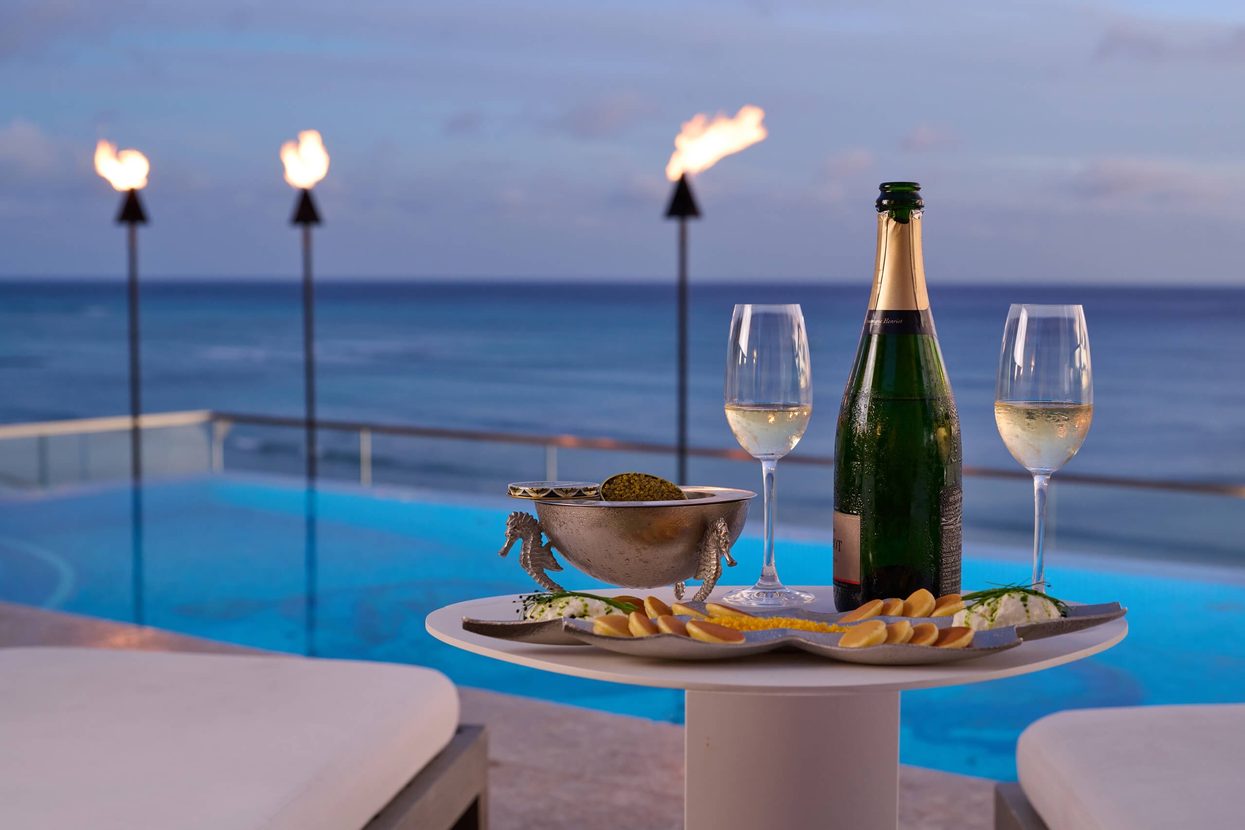Champagne and caviar service at the rooftop pool deck at sunset, tiki torches lit