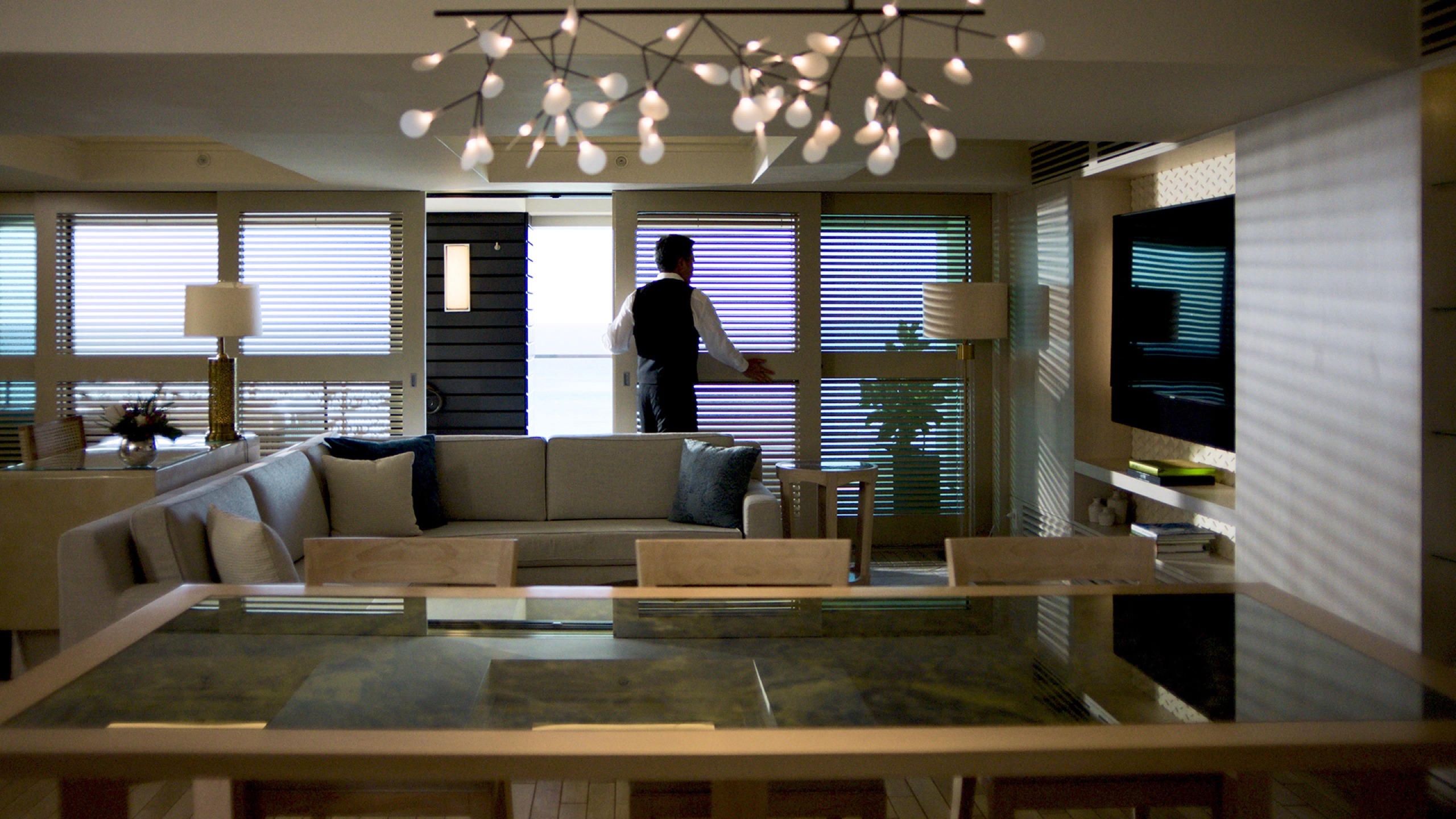 Suite living room with chandelier, butler at the window, ocean beyond